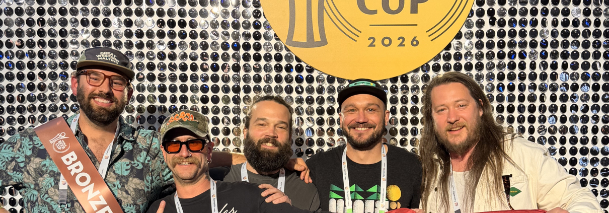 Hi-Wire staff at the 2026 World Beer Cup with smiling faces pose in front of a WBC backdrop while holding the state flag of North Carolina